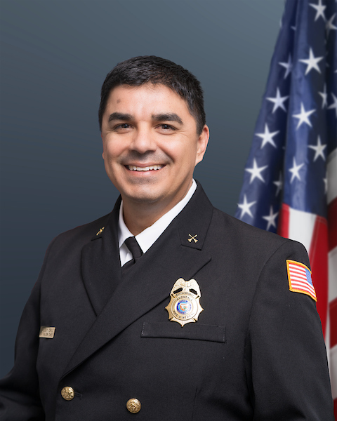 Battalion Chief Freddy Cruz wearing his class "A"s with an American flag behind him